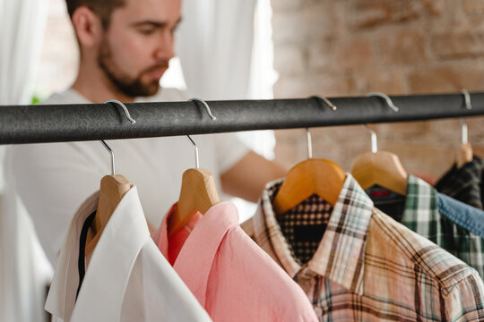 Man is browsing through his various shirts hanging on the clothing rack in the wardrobe