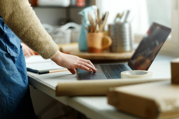 Cropped woman in apron working with laptop in studio. Small business and entrepreneurship in art,...