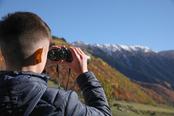 Boy looking through binoculars in mountains on sunny day. Space for text