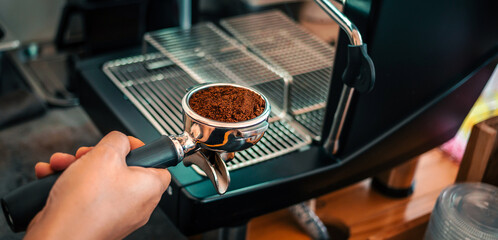 ground coffee powder in portafilter and coffee tamper making an espresso coffee in the barista's hand
