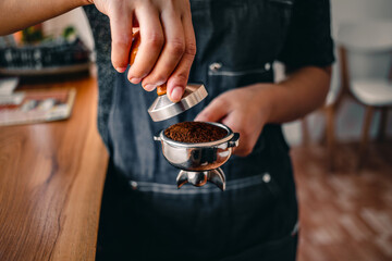 Close-up of hand barista or coffee maker holding portafilter and coffee tamper making an espresso coffee.