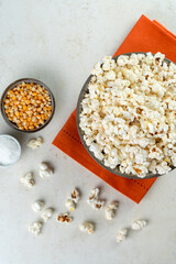  bowl with popcorn, popcorn kernels and salt on an orange napkin, on a marble table, top view