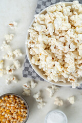 Glass bowl with popcorn, popcorn kernels and salt on a marble table, top view, selected focus