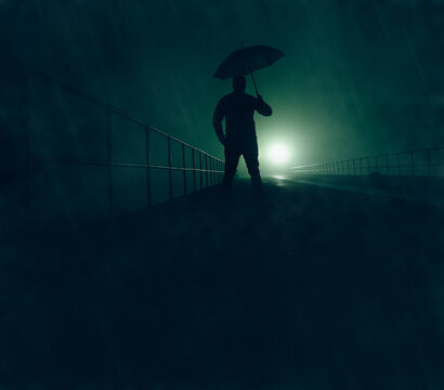 A mysterious man in silhouette, standing on a bridge in the rain, with a light in the distance illuminating the fog 