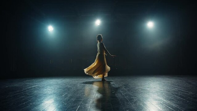 Young woman ballet dancer dances on stage in flowing dress. Choreographer setting ballet performance dancing on spotted stage