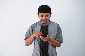 Happy or smiling young asian muslim man holding and pointing on phone cellular wearing koko clothes...