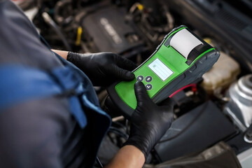 Male auto mechanic with an electronic device for checking a car in a car service garage. Car maintenance and repair