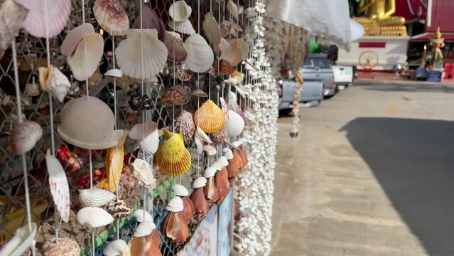 Beautiful seashell mobile hanging decoration for sell close up shot sunny day inside buddhist monastery with view of blurred buddha statue and cars in background. Tourism and travel concept, Thailand
