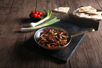 Beef meat stew in a pan and served with bread, green onion, and cherry tomato on a wooden table