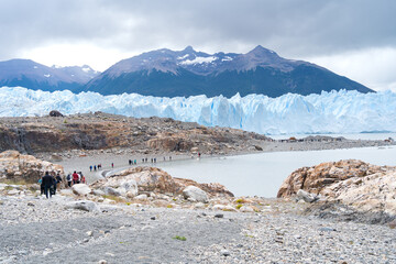 Grandes grupos de personas se dirigen caminando cerca de la playa hacia el glaciar Perito Moreno para realizar trekking.