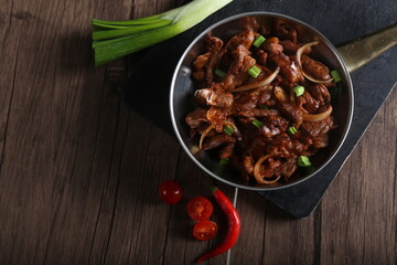 Beef meat stew in a pan and served with bread, green onion, and cherry tomato on a wooden table