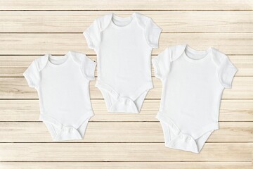Three different size baby bodysuits, set of white cotton bodysuits mockups for design presentation, wooden background.