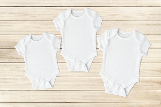 Three different size baby bodysuits, set of white cotton bodysuits mockups for design presentation, wooden background.