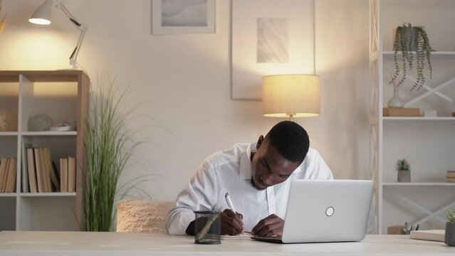 Webinar learning. Professional study. Remote education. Serious man employee writing notes watching laptop tutorial lesson at home desk.