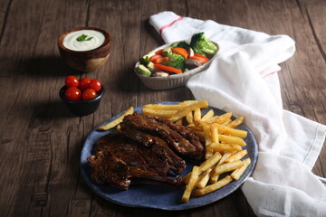 Grilled steak with french fries served with vegetables, cherry tomatoes, and garlic sauce on a plate on a wooden table