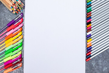 Set of colorful pens and pencils with blank sheet of paper on grey background
