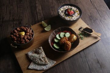 Wooden tray served with Egyptian breakfast contains beans with a butter slice, fried eggs with vegetables, tomato cheese, lemon slices and bread.