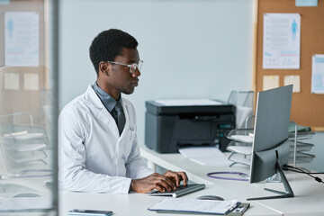 Young black doctor using computer at desk in office working in clinic