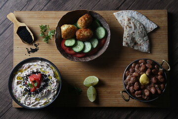 Wooden tray served with Egyptian breakfast contains beans with a butter slice, fried eggs with vegetables, tomato cheese, lemon slices and bread.