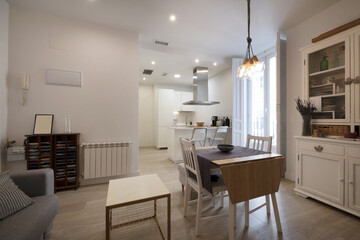 Naklejka na ściany i meble Living room furnished with a folding table in the center of a vacation rental apartment with access to an open plan kitchen with a balcony with white wooden doors