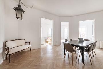 Living room with an elongated armchair in a corner, a vintage wooden table with wheels on its legs and several accesses to other rooms without doors