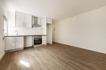 Kitchen open to newly installed empty living room that is missing some appliances with wooden flooring