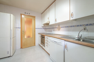 Modest kitchen with cheap flooring with built-in appliances and a fridge in a corner with a wooden...