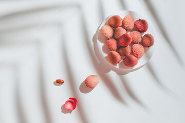 Minimal style composition made of fresh lychee fruits on white background with palm tree leaf shadow. Summer refreshment concept. Still life. Top view