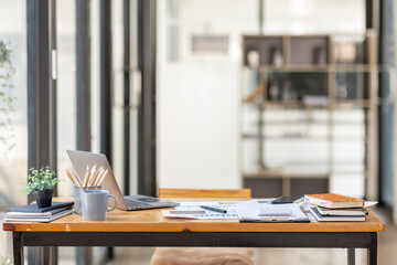 Laptop Computer, notebook, and eyeglasses sitting on a desk in a large open plan office space after...