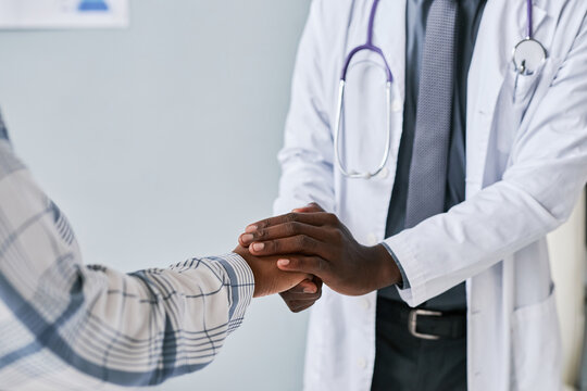 Close up caring black doctor holding hands with female patient