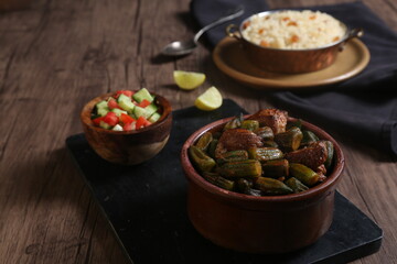 Egyptian okra casserole served with lemon, salad, and Egyptian rice with tahini and garlic on a black tray