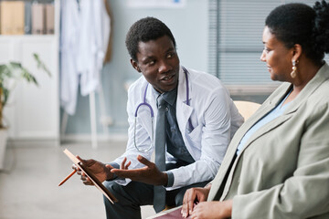 Black young man as doctor consulting female patient in clinic