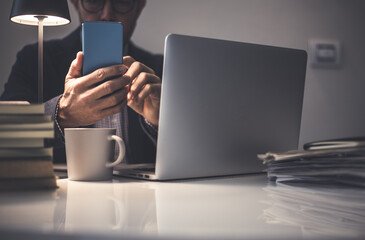 Businessman working with laptop, smartphone in hand. Documents, mug and books on the desk.