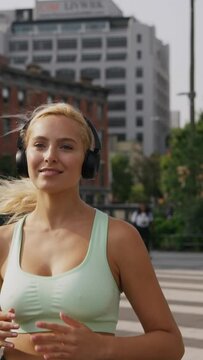 Young fitness sport woman running and listening music in headphones on city road