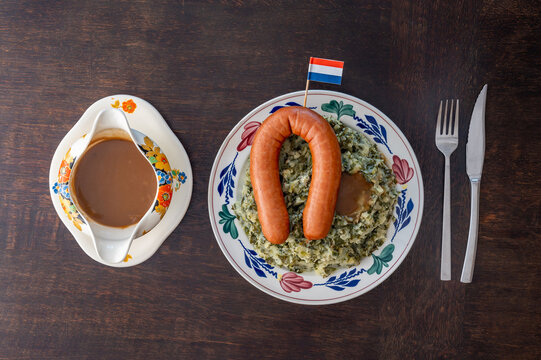 Portion of traditional dutch 'Boerenkool stamppot met worst' potatoes mashed with kale, smoked sausage and gravy on a plate with dutch flag