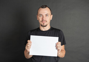 Young handsome man holding empty white sheet of paper
