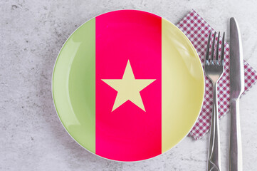 A Plate with the Flag of Cameroon, Cutlery and Napkins on the Mable Table.