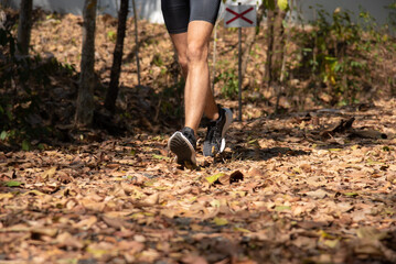 Closeup selective focus of feet runner jogging workout. Marathon runner sport shoes tying shoelace, exercising outdoors workout on forest dirt road. Athlete endurance trail running.