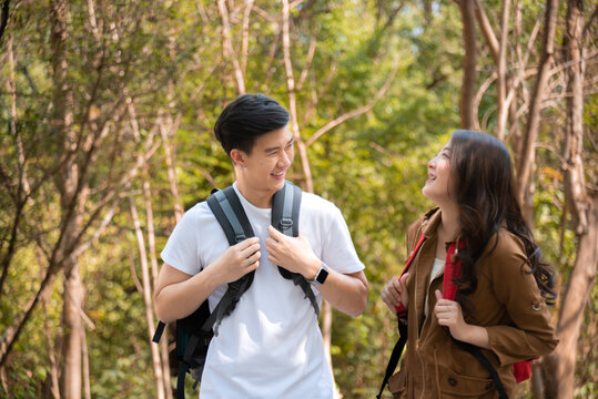 Happy love couple take photo and selfie during camping and relax in forest hiking trip, beautiful Asian woman and handsome man happiness spend time tpgether, sunset liesure romantic moment