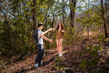 Young Asian tourists couple climbing on rock, woman helping hand man hiking looking view beautiful nature outdoor. Partner or couple adventure travel together in forest summer stand on peak mountain.