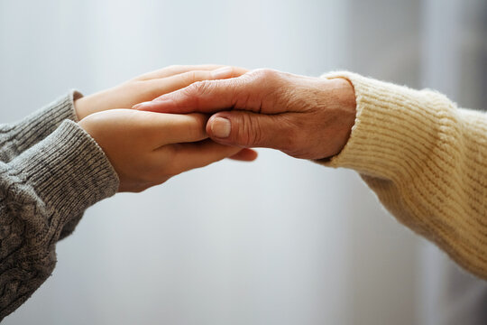 Closeup Of Hand Of Old Woman And A Young Female Hands. Senior Woman, With Caregiver Indoors. Helping Hand For The Elderly Concept With Young Hands Holding Old Hand.