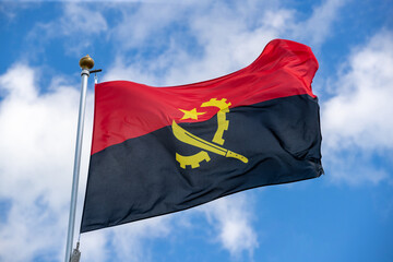 Naklejka na ściany i meble The flag of Angola in the beautiful sky flutters the fabric of the national flag of Angola. Great for news