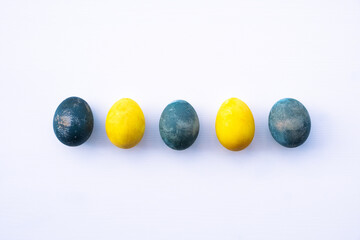 Natural dyed blue and yellow colored eggs on white background, top view, flat lay. Happy Easter. Copy space for text.