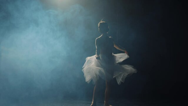 Portrait of young woman ballerina dancing in spotlight on stage. Ballet dancer silhouette in pointe shoes