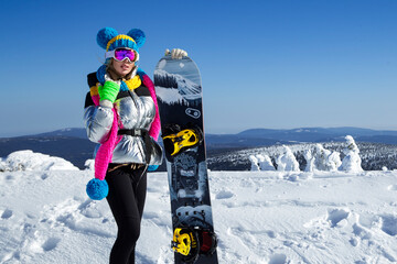 Girl snowboarder enjoys the ski resort. Beautiful woman in winter outfit is posing with snowboard...