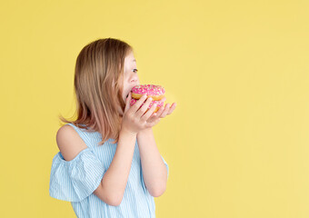 Portrait of a lovely young girl eating donuts isolated over yellow background