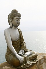La statue d'un Bouddha assis sur un muret au bord de la mer