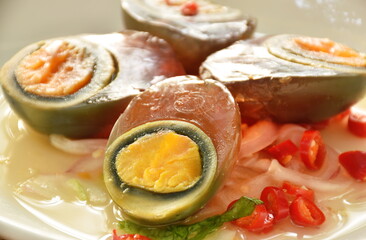 boiled salty black preserved egg half cut with slice shallot salad on plate