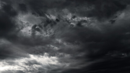 Obraz premium dark dramatic sky with black stormy clouds before rain or snow as abstract background, extreme weather, the sun shines through the clouds, high contrast photo