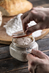 Male hands open a jar with active yeast, flour and fresh bread and pastries in the background